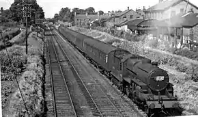 Photo noir et blanc, voie ferrée, train à vapeur, maisons sur les berges.