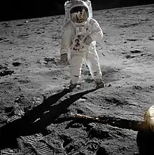 Un astronaute regarde la caméra, le sol est désertique autour.