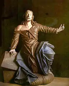 Photographie en couleurs. Statue colorée de Jésus en pied, agenouillé et le bras levé vers le ciel en position d'imploration.