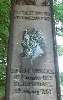 Photographie d'un mémorial funéraire, un visage de profil est gravé sur une plaque de cuivre.