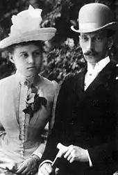 Portrait en buste d'un jeune couple. La femme porte une robe claire et un chapeau blanc ; l'homme moustachu porte un costume noir et une chapeau melon.