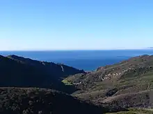 Une large vallée entre des colinnes arides couvertes de chaparral, s'ouvrant vers l'océan Pacifique.