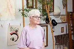 Une femme âgée devant des dessins accrochés au mur