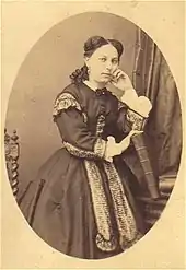 Portrait en médaillon d'Alix Payen. Elle est de face, debout et se tient le visage en étant accoudée sur un dossier de siège. Elle est vêtue d'une robe et a les cheveux longs et tressés.