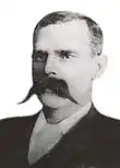 Photographie d'un homme d'age mur en costume sombre avec une impressionnante moustache couvrant sa bouche et une bonne partie de ses joues.