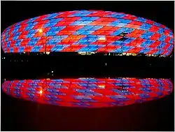 Photographie d'un stade de football, vu de l'extérieur, avec des couleurs rouges et bleues.