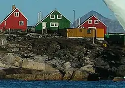 Photographie en couleurs de trois maisons et d'un bâtiment en bois surplombant la mer.