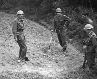 Photographie de quatre hommes en uniforme sur ou à proximité d'un tas de gravats. L'un d'eux s'appuie sur une pelle.