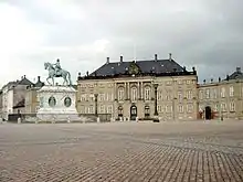 Une vaste place pavée avec, en arrière plan, une statue équestre et un palais de style néo-classique.