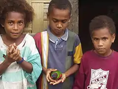 Photographie représentant trois enfants, dont un garçon tenant un perroquet.