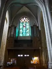 Photographie couleur de la tribune portant orgue et de la verrière en lancette d'une église gothique.