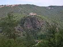 photo couleur d'un hameau avec un clocher au sommet d'une crête rocheuse cernée de pentes abruptes couvertes de forêt.