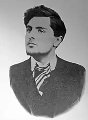 Photo noir et blanc d'un jeune homme en buste menton relevé un peu vers la droite, costume sombre et large cravate rayée