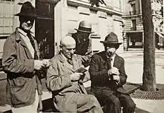 Photo noir et blanc de quatre hommes autour d'un banc, le premier et le troisième assis