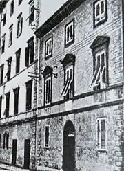Photo noir et blanc et de côté d'une façade de maison en pierre avec porte arrondie et jalousies aux fenêtres