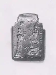Petite tablette carrée de pierre noire polie et sur laquelle sont gravés deux personnages face à face et un animal placé sous le personnage de droite qui est assis.