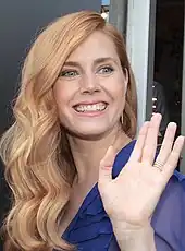 Photographie d’une jeune femme saluant une personne en souriant.