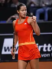 Une joueuse de tennis en combinaison orange serre le poing.