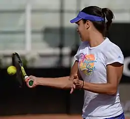 Une joueuse de tennis en action frappant la balle avec sa raquette. Ses deux bras sont tendus à angle droit et sa main libre est détendue.