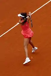 De dos, une joueuse de tennis en robe rose en action sur un court de terre battue.