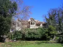 Photographie en couleur d'une vaste villa en partie cachée par la végétation.