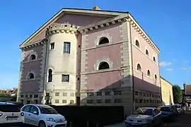 Photographie en couleurs d'un bâtiment à étages en maçonnerie rose. Tour semi-cylindrique engagée dans la façade.