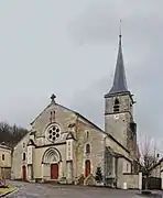 Façade à collatéraux et trois portes rouges, le clocher carré à longue flèche est en retrait sur le transept.