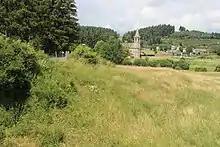 Photographie en couleurs d'un terrain vallonné avec une église en arrière-plan.