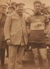 Photographie d'un coureur cycliste en tenue posant à côté d'un homme en costume.
