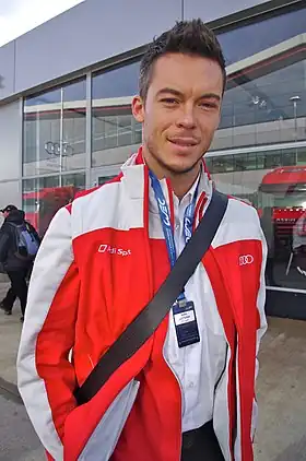 Homme brun habillé en rouge et blanc, vu de face, souriant.