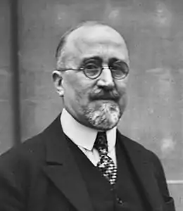 Portrait photographique en noir et blanc d'un homme souriant légèrement, portant des lunettes rondes.