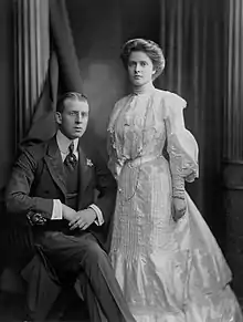 Photographie en noir et blanc d'un jeune couple, le mari assis et la femme debout.