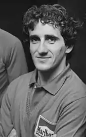 Photo en noir et blanc resserrée en portrait sur Alain Prost, prenant la pose, de face.
