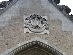 Photographie d'un bas-relief mural représentant deux lions encadrant deux écussons surmontés d'une couronne, avec inscription latine.