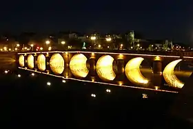 Photographie d'un pont à arches rondes éclairé la nuit.