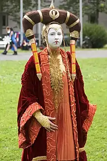 Femme déguisée dont le visage est peint en blanc et porte une robe rouge très ouvragée.