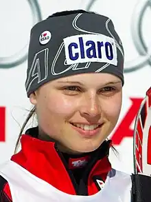 Portrait d’une jeune femme, souriante, vêtu d’une veste de ski rouge et d’un bandeau gris, avec une publicité