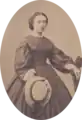 Photographie ancienne d'une femme en robe, tenant un chapeau de paille.