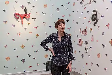 Une femme artiste devant un mur avec de nombreux dessins colorés d'utérus.