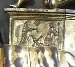 Détail de bas-relief en bronze. Un personnage debout s'adresse à une femme assise, les bras croisés sur la poitrine.