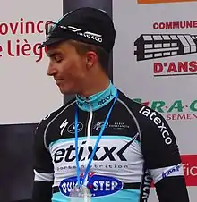 Photo d'un homme debout, de profil, portant une casquette, devant un panneau publicitaire.