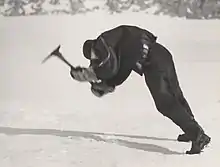 Un homme en tenue polaire se penche face à des vents violents tout en essayant d'utiliser un piolet.