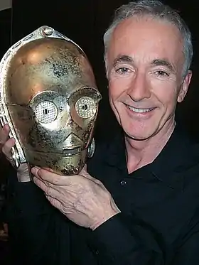 Homme aux cheveux gris portant une tête de robot doré.