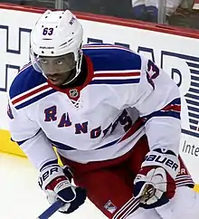 Photographie couleur d’un hockeyeur, de cuisse, penché sur sa droite et en avant, le regard en l’air