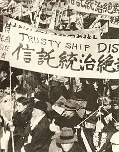 Photographie d'une foule en train de manifester, portant des écriteaux en anglais et en chinois.