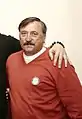 Photographie d'un homme brun avec une moustache noire, vu de face, avec un maillot rouge.