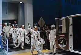 Photographie en couleur des astronautes d'Apollo 11 se rendant au pas de tir en saluant les photographes.