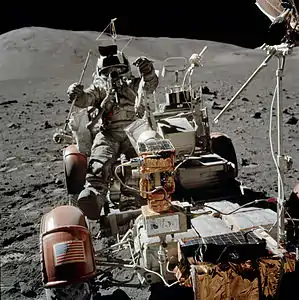 Avant du rover. Schmitt réintègre le rover en effectuant un saut ; il tient à la main l'outil lui permettant de collecter des échantillons sans descendre du rover.