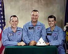 Photographie en couleur de trois hommes posant en combinaisons bleues.