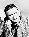 Photographie en noir et blanc de Borman souriant au téléphone.